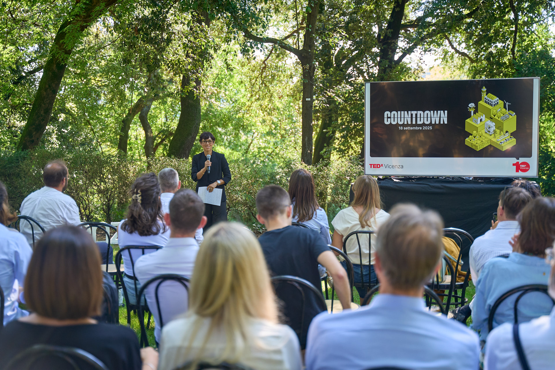 Pubblico riunito all’aperto in un’area verde per TEDxVicenza Countdown 2025, con un relatore davanti a uno schermo che presenta l’evento del 18 settembre 2025.