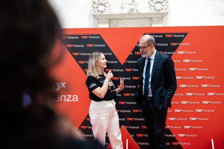 Intervista durante il TEDxVicenza Main Event 2025, con una giovane intervistatrice e un uomo in abito davanti a un backdrop rosso e nero con il logo TEDxVicenza.