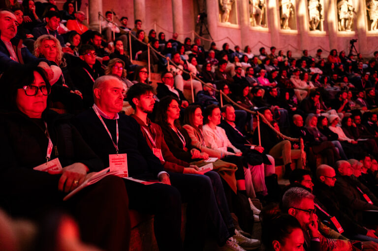Pubblico del TEDxVicenza Main Event 2025 seduto sulle gradinate di un teatro storico durante l’evento, illuminato dalle luci rosse della scenografia.