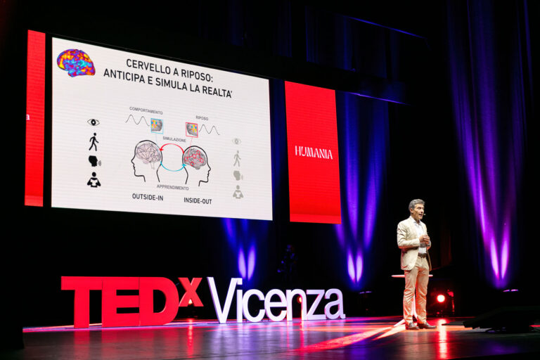 Speaker sul palco del TEDxVicenza Main Event 2024 durante un intervento sul tema Humania, con una presentazione sul cervello e la simulazione della realtà proiettata sullo schermo.