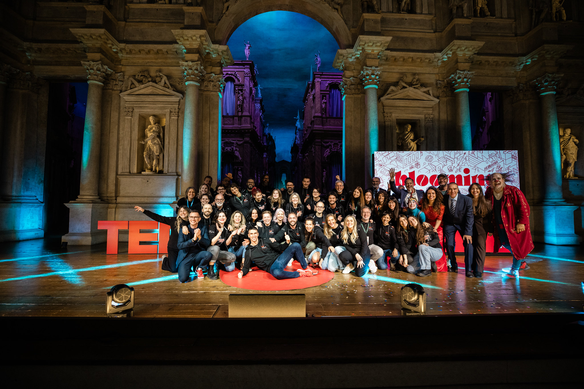 Gruppo di organizzatori e partecipanti riuniti sul palco di un TEDxVicenza Main Event 2025, davanti al grande logo TEDx e a una scenografia illuminata con luci colorate in un teatro storico.